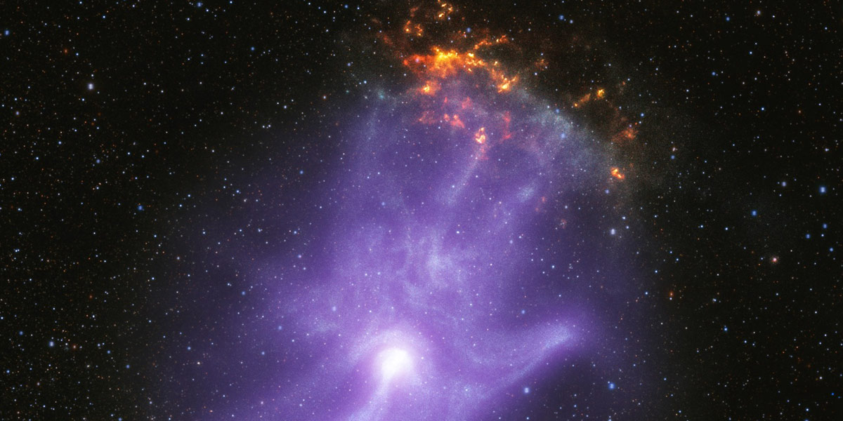 Composite image of MSH 15-52, a pulsar wind nebula, which strongly resembles a ghostly purple hand with sparkling fingertips. The hazy purple cloud is set against a black, starry backdrop. The bright white spot near the base of the palm is the pulsar. The three longest fingertips of the hand-shape point toward 1 o’clock. There, a small, mottled, orange and yellow cloud appears to sparkle or glow like embers. This orange cloud is part of the remains of the supernova explosion that created the pulsar.