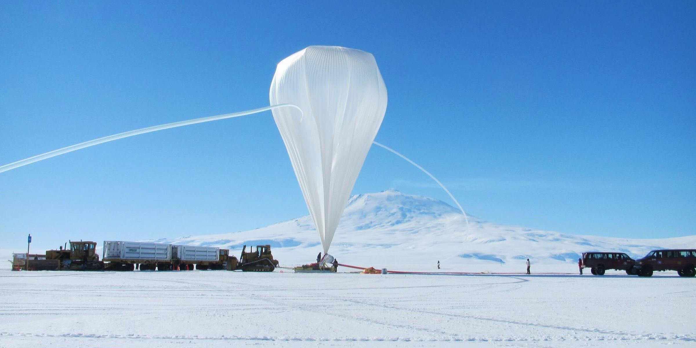 NASA's GUSTO mission preparing its white stratospheric balloon in snow-covered Antarctica against a sky with a bright blue hue.