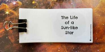 A printed horizontal series of white pages are clipped together at left by a black binder clip. The title on the first page, "The Life of a Sun-like Star" appears at right, with much smaller text running vertically, NASA's universe of Learning. The paper is set against a star field filled with stars and irregular layers of brown gas.