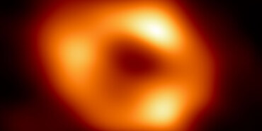 Event Horizon Telescope image of the black hole at the center of the Milky Way galaxy, Sagittarius A. It resembles a slightly oblong donut-shaped ring of glowing, warm dust. Within the ring, there are especially bright areas at the top, left, and right.